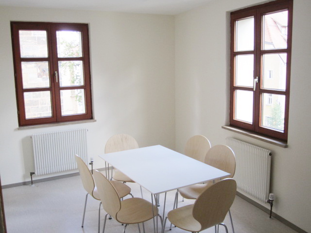 Gemeinschaftsraum mit Esstisch und sechs Stühlen an zwei Holzfenstern – Studentenwohnheim Eichenforst Amberg