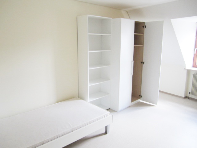 Möbliertes Zimmer mit Bett, offenem Regal und Kleiderschrank unter der Dachschräge – Studentenwohnheim Eichenforst Amberg
